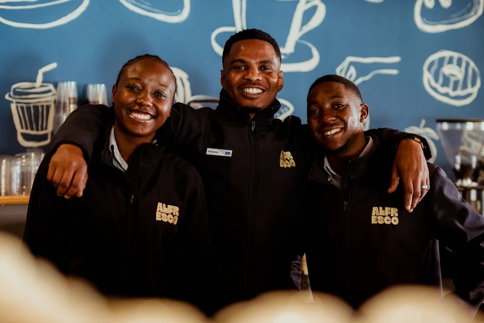 Three Alfresco team members smiling behind the counter