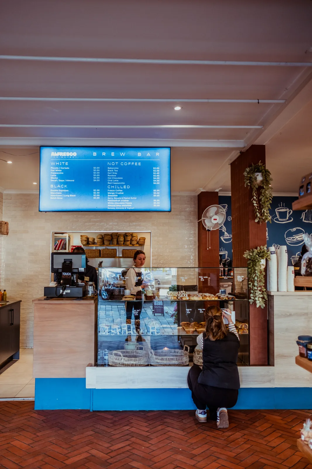 Alfresco employee behind the counter while someone writes beside the glass display