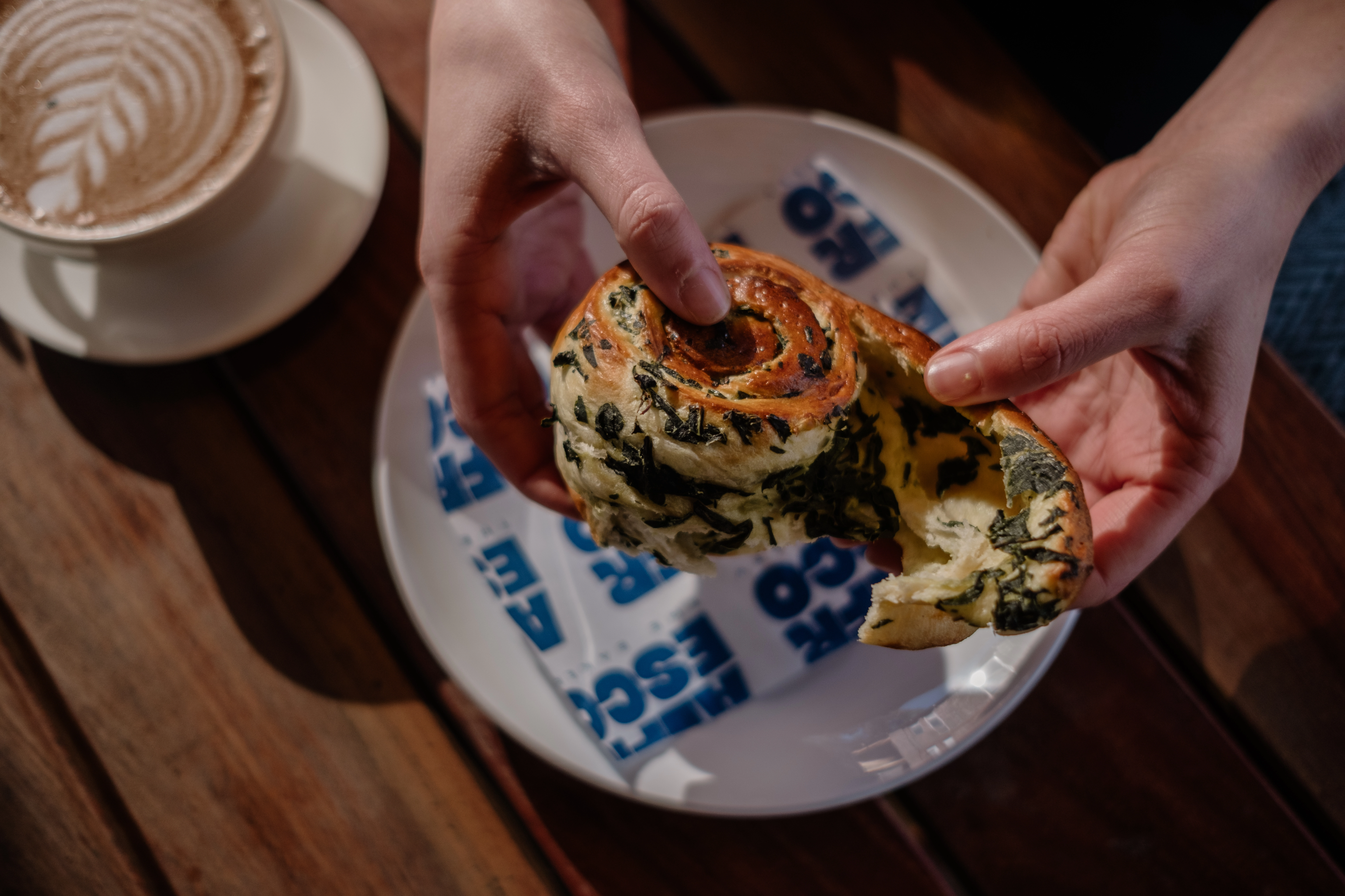 Savoury bun being broken with plate and coffee in background, aesthetic styling